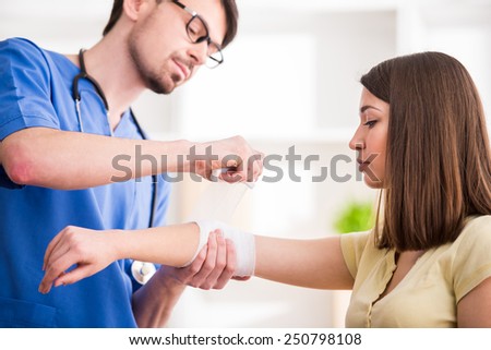 Confident male doctor is bandaging upper limb of young woman.