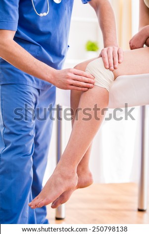 Doctor is rewinding knee bandage to young woman.