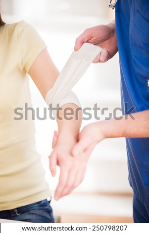 Young man is bandaging upper limb of beautiful woman.