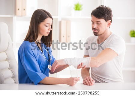 Pretty female doctor is bandaging upper limb of young man.