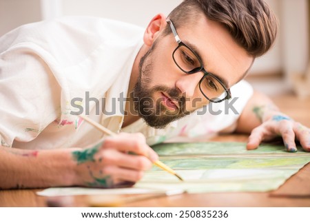 Young artist is painting on canvas is lying on studio floor. Close-up.