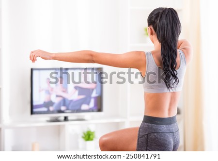 Rear view of a young woman doing home exercises while watching program on television