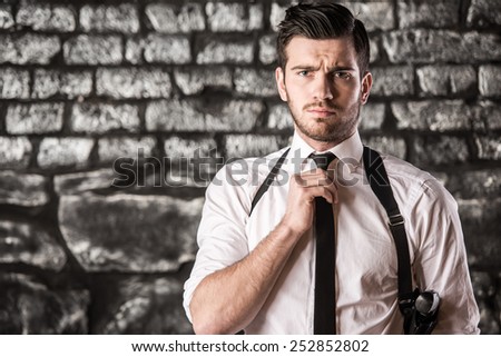Portrait of a young, serious man is posing near a wall with a gun.