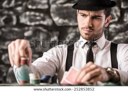 View of young, confident, gangster man in shirt, suspenders and hat, while he\'s playing poker game.