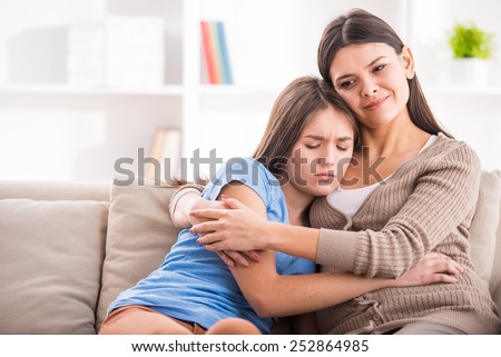 Mother and teen daughter are hugging after quarrel on sofa at home.