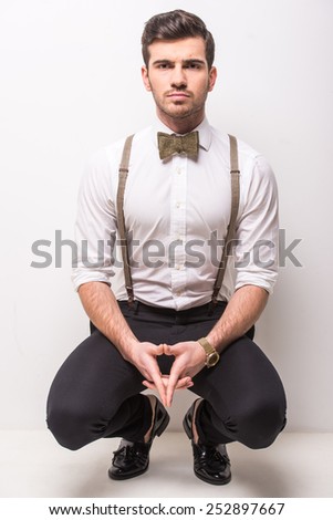 Young trendy man with black glasses, suspenders and bow-tie on gray background.