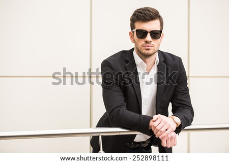 Portrait of young trendy man with black glasses is posing in front of a wall.