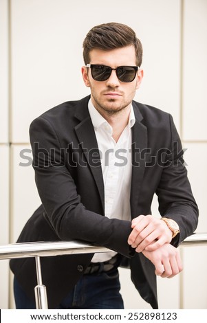 Portrait of young trendy man with black glasses is posing in front of a wall.