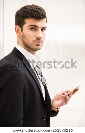 Close-up of handsome man with smartphone on the light background is looking at the camera.