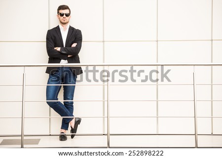 Portrait of young trendy man with black glasses is posing in modern office.