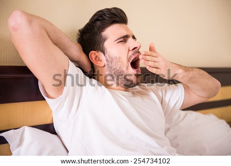 Young handsome man is waking in morning. Attractive guy is stretching and yawning in bed.