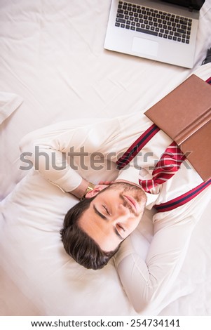 Top view of young handsome man is sleeping on bed in suit.