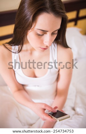 Top view of young woman is looking at the phone, sitting on bed at morning.