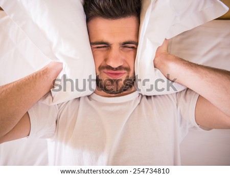 Young man is trying to sleep with a pillow over his head.