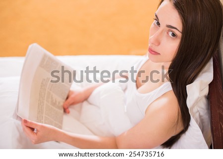 Top view of young woman is reading a newspaper, sitting on bed at morning.