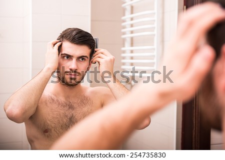 Morning hygiene. Handsome man is combing his hair, looking at the mirror.