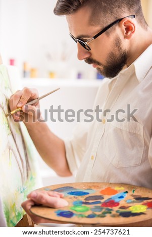 Portrait of highly gifted painter is holding brush and palette in his hand is finishing his picture.