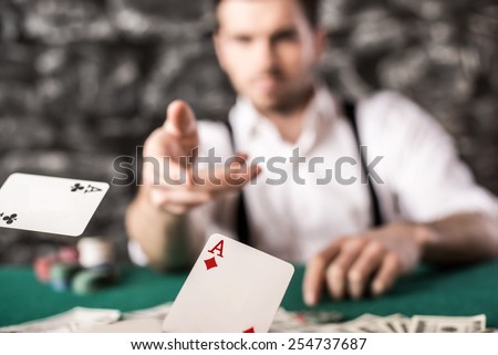 Young, confident, gangster man in shirt and suspenders, is throwing his cards on poker table, while he\'s playing poker game.