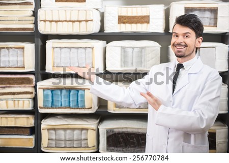 The young salesman is showing quality mattresses in the store.