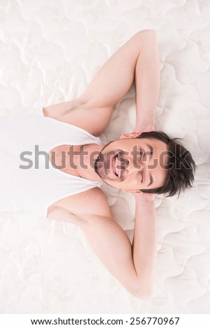 Young man is lying on the quality mattress and looking at the camera, over white background