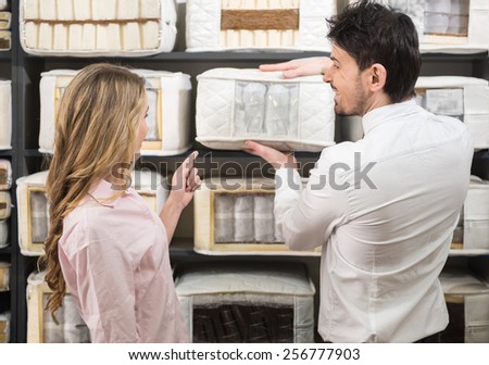 The young salesman tells the customer about quality mattresses in the store.