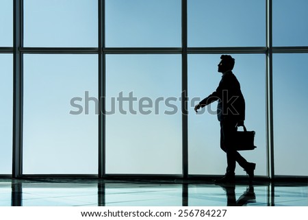 Silhouette view of young businessman is standing in modern office with panoramic windows.