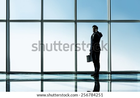 Silhouette view of young businessman is standing in modern office with panoramic windows.