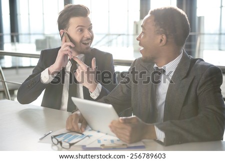 Young black smiling businessman is looking at his partner who talking by phone.
