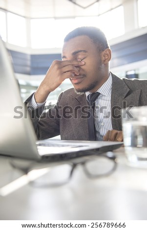 Young black tired businessman is sitting at the table and working in modern office.