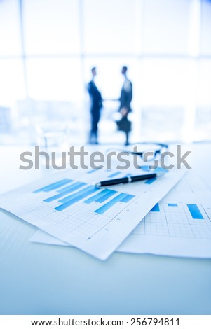 Focus on the things on the table. Blurred men near panoramic windows on background.