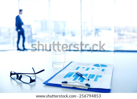 Focus on the things on the table. Blurred man near panoramic windows on background.