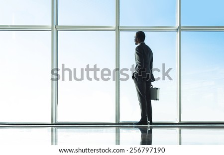 Back view of young businessman is looking out of a panoramic window and talking by phone.