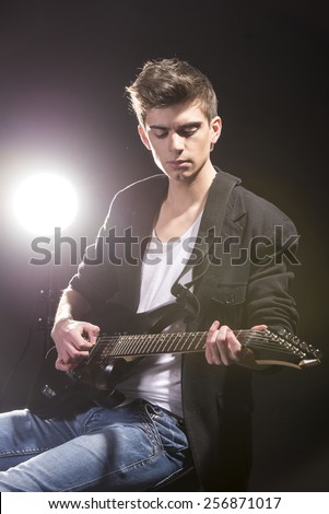 Guitar player. Young man with guitar in dark room with lights behind him.