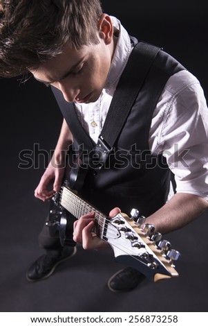Top view of young male musician is playing a six-string bass guitar isolated on dark background.