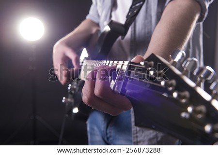 Guitar player. Close-up hands of young man is playing guitar in dark room with lights behind him.