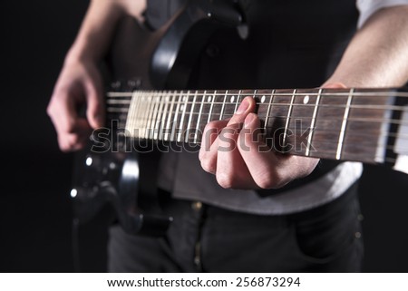 Close-up hands of young guitarist with the electric guitar, isolated on dark background.