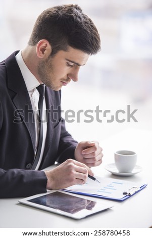 Young businessman is working with papers and drinking coffe.
