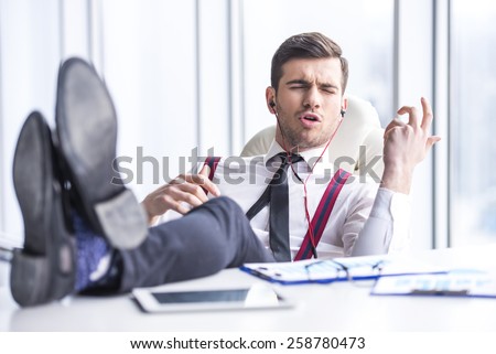 Young man in suit is listening music in headphone in office.