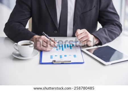 Young businessman is working with papers and drinking coffe.