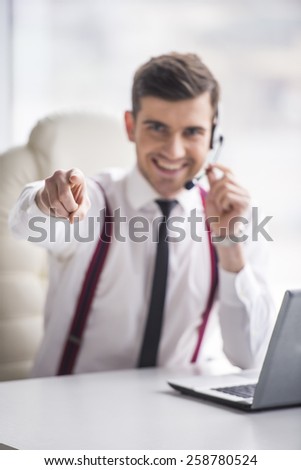 Smiling businessman is taking a call on a headset as he deals with queries at the customer support call centre.