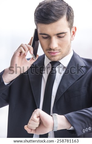 Businessman is looking at his watch while taking a call.