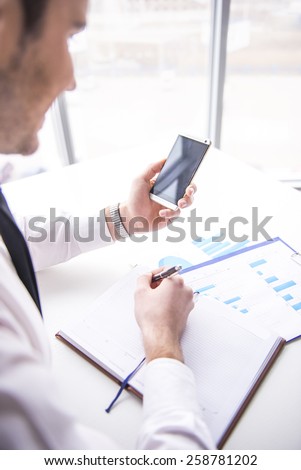 Businessman is using mobile phone at desk in  office. Side view of.