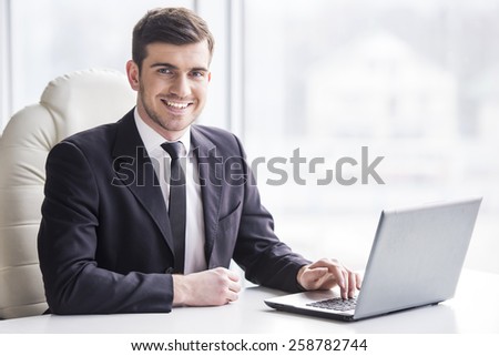 Handsome businessman is working with laptop in office is looking at the camera.