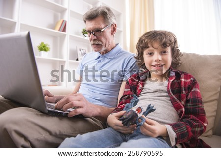 A boy is holding a toy in hands at the older man working on a laptop