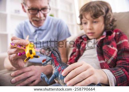 A preschooler and his grandpa happily are playing with toy dinosaurs.