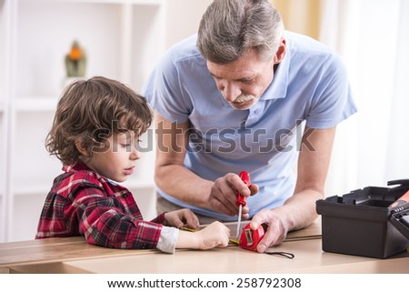 Grandfather and grandson are measuring a board with measuring tape.