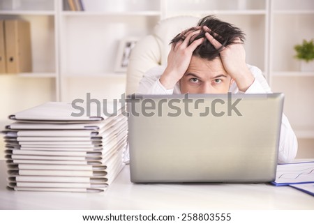 Frustrated middle aged businessman sitting at office desk and looking at camera