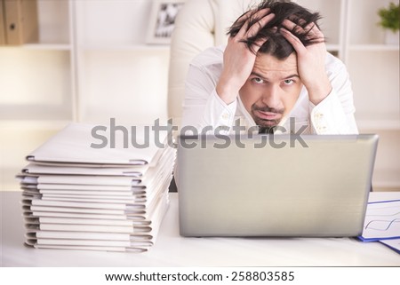 Frustrated middle aged businessman sitting at office desk and looking at camera