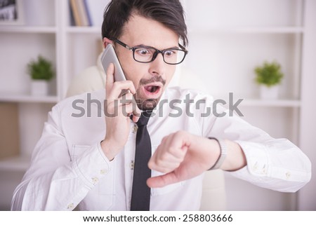 Socked businessman is speaking by phone and looking at the clock.
