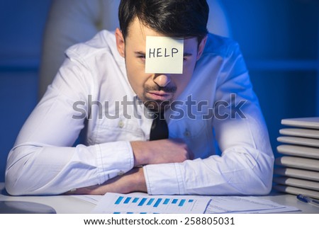 Frustrated young businessman in his office with adhesive note on his forehead. He needs help.